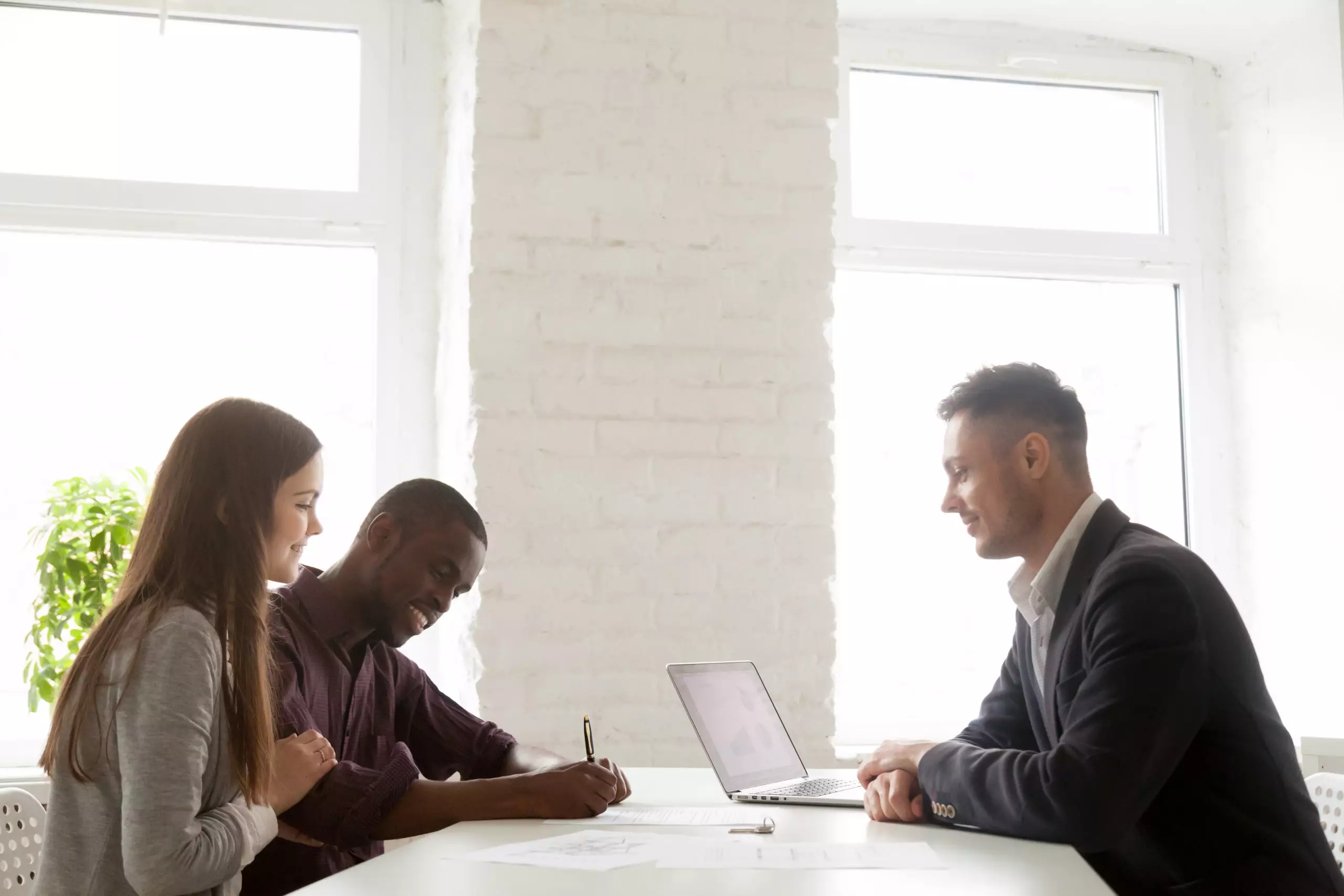 Multiethnic young spouses signing contract on property purchase while visiting real estate agent